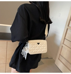 Detail of cream quilted leather camera bag with metal logo and lace bow on a model