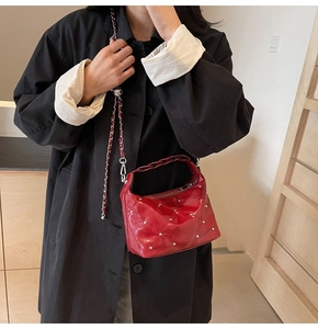 Detail of red quilted patent leather bag with silver studs and chain strap shown on model