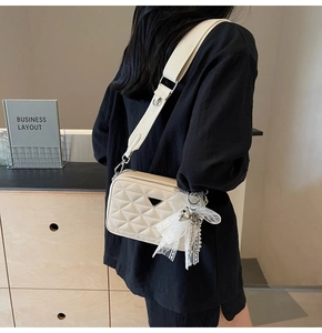 Detail of beige quilted camera bag featuring elegant lace bow and pearl pendant charm