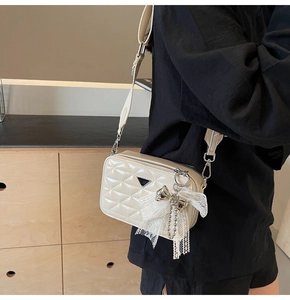 Detail view of cream quilted faux leather bag with lace bow charm and wide fabric strap