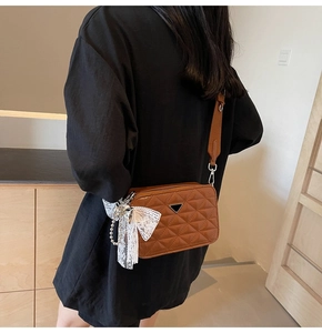 Detailed view of brown quilted camera bag with elegant bow and pearl pendant charm