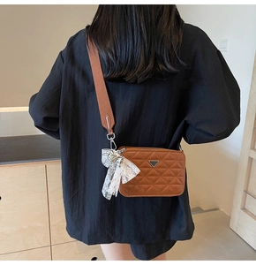 Brown quilted camera bag with wide fabric strap and delicate lace bow charm detail