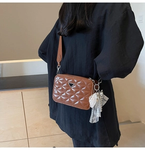 Detail of brown quilted camera bag with glossy finish and decorative lace bow charm