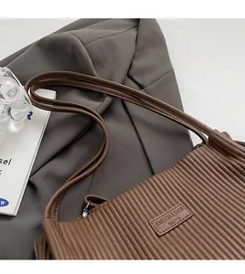 Macro detail of brown pleated leather shoulder bag with textured finish and slim straps
