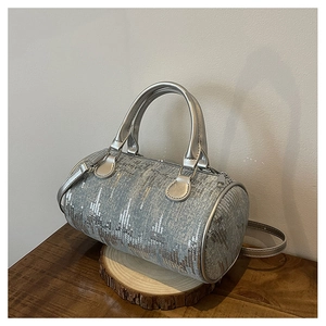 Close-up of silver sequined barrel bag on wooden base showing texture and metallic handles