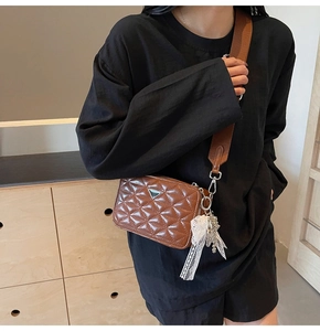 Detail of a brown quilted camera bag with a wide strap and lace charm on a shoulder