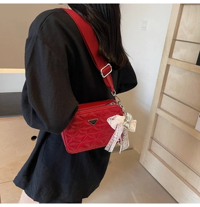 Detail of red quilted camera bag with wide strap and white lace bow accessory