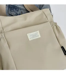 Close-up of beige lightweight nylon shoulder bag with a square fabric logo patch
