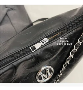 Close-up of smooth silver zipper and metallic logo on black crinkled leather tote bag