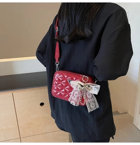 Detail of red quilted patent leather camera bag with lace bow charm and metal logo