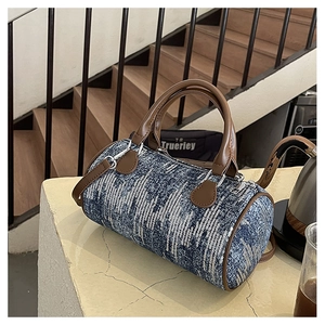 Detail showing the denim-style texture, brown leather handles, and silver zippers of the bag