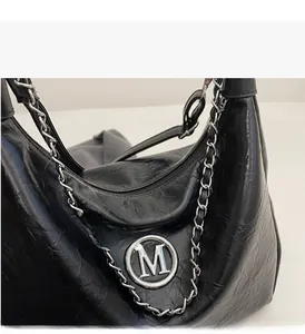 Detail of black wrinkled tote bag with silver chain and metal M logo charm