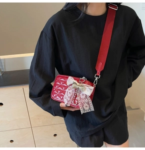 Close-up of a red quilted leather crossbody bag with white lace bow detail and wide strap