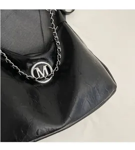 Detailed close-up of black pleated faux leather and silver M logo chain strap
