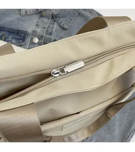 Detail view of smooth metal zipper and light brown nylon strap on beige crossbody bag