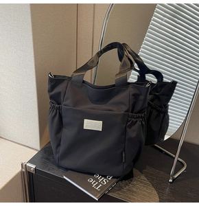 Detail of a black nylon tote bag with side drawstring and branded square logo patch