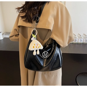 Detail of black glossy leather tote with M logo and plush toast charm accessory