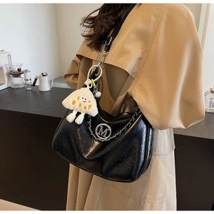 Close-up of black pleated tote bag with silver chain M-logo and white plush charm detail