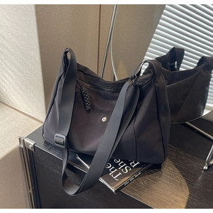 Dettaglio di una borsa tote in nylon nero con tracolla regolabile e bottone a pressione