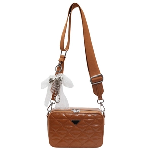Brown quilted leather camera bag with a wide strap and lace bow charm on white background