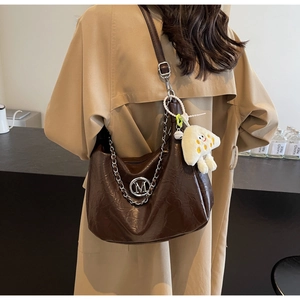 Close-up of brown crescent bag with metal chain and cute plush elf charm detail