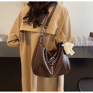 Detail of dark brown croissant bag with chain and plush charm on trench coat
