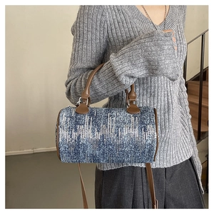 Cylindrical denim pillow bag with silver sequins and brown leather straps on a model