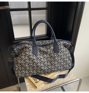 Detail of blue geometric canvas travel bag with leather handles on marble table