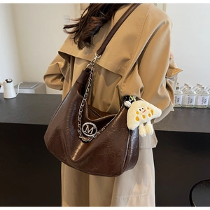 Detail of coffee brown tote bag featuring metallic M logo and chain strap on shoulder