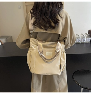 Detail of beige nylon tote bag featuring side drawstring pocket and metal-gloss straps