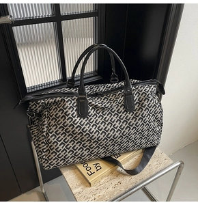 Close-up of a travel bag featuring grey geometric H-pattern and black leather handles