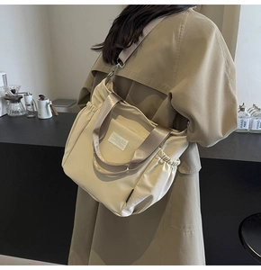 Detail of beige nylon tote bag featuring side drawstrings and adjustable shoulder strap
