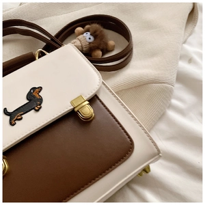 Close-up of beige and brown leather bag featuring dachshund embroidery and gold clasp