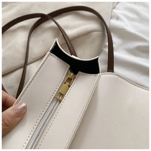 Close-up of premium cream leather handbag with gold metal zipper and dark brown strap