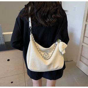 Detail of off-white pleated shoulder bag with M-logo, silver chain, and plush pendant