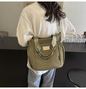 Waterproof olive green nylon tote bag worn as a shoulder bag in a modern cafe setting