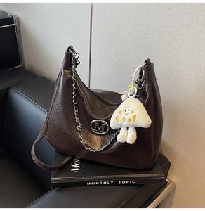 Close-up of dark brown crescent chain bag with crinkled leather and plush mushroom charm