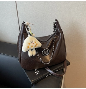 Detail of dark brown crinkled leather bag with silver chain and plush mushroom charm