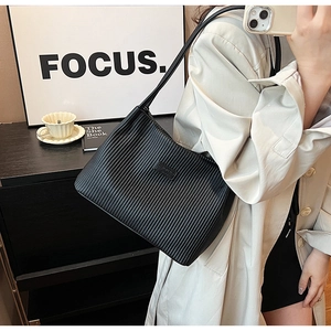 Detail of black tote bag with vertical pleat texture and elegant rectangular logo plate