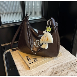 Detail of dark brown glossy tote bag with silver M logo and plush mushroom charm