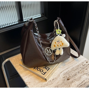 Detail of coffee hobo bag with M logo, silver chain and white plush charm on books