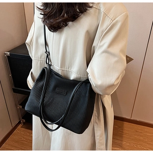 Detail of black pleated PU leather tote bag with brand logo and adjustable strap