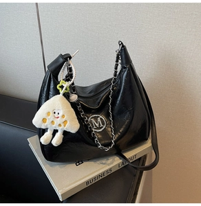 Detail of black pleated tote bag with silver M logo, metal chain and plush charm