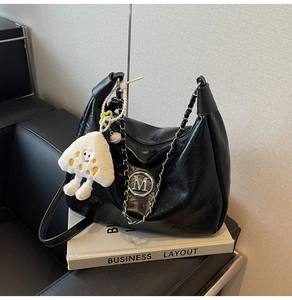Close-up of black pleated faux leather bag with silver M hardware and white plush charm