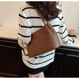 Detail of a brown pleated tote bag with a small logo tag worn on a striped sweater