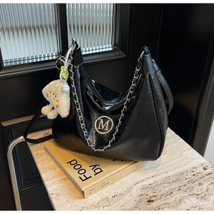 Detail of glossy pleated leather bag featuring silver M logo and white plush charm