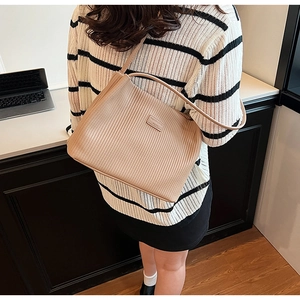 Close-up of beige tote bag featuring vertical pleated texture and leather brand patch