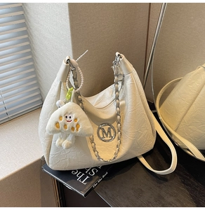Detailed shot of white pleated tote bag featuring silver M logo and plush mushroom charm