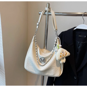 Detail of cream crescent shoulder bag with metallic M logo and plush monster charm