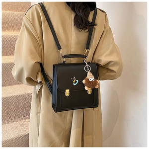 Detail of a black square backpack with gold buckles and a cute plush toy pendant charm